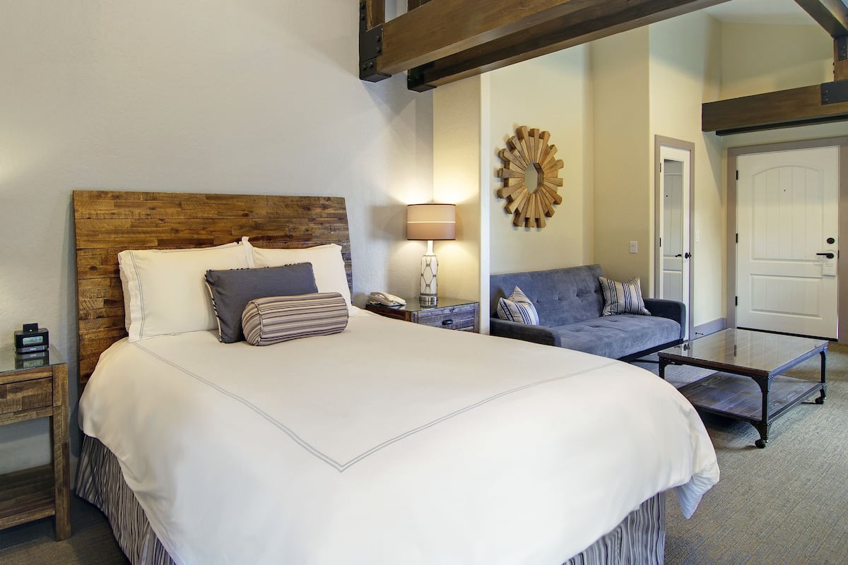 A hotel room with a large bed, bedside tables, a sofa, and a mirror.