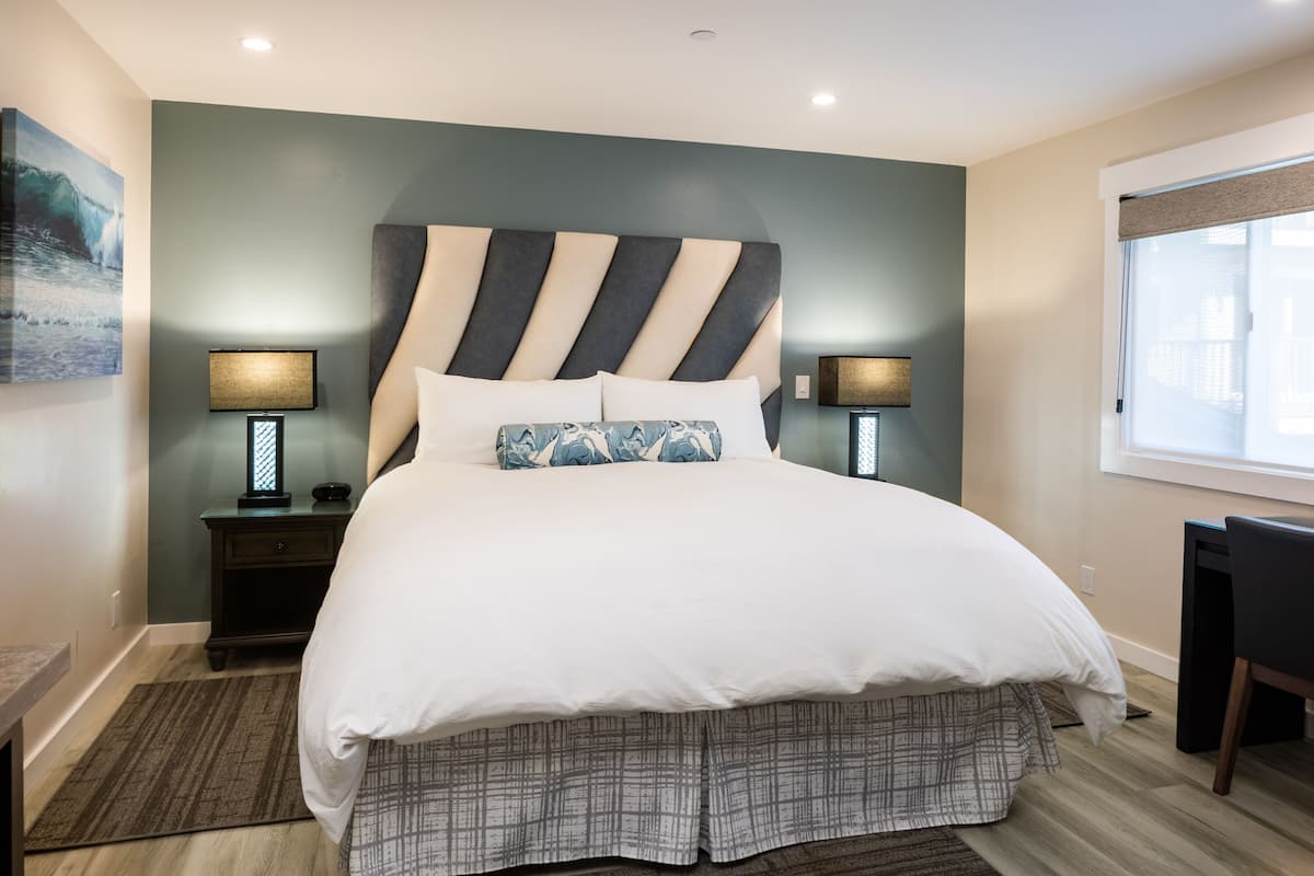A modern bedroom with a large bed, two bedside lamps, a headboard, and a view of the outside through a window.