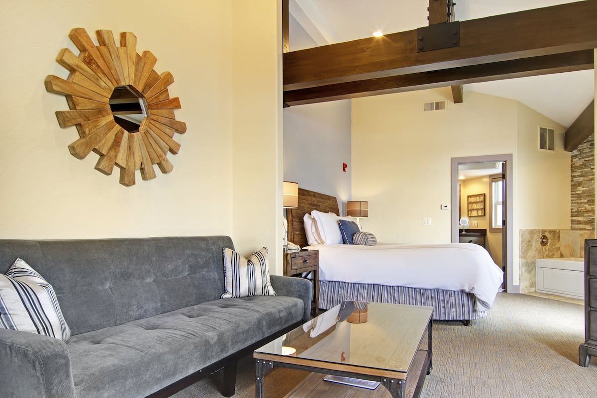 A hotel room with a large bed, a gray sofa, a wooden accent wall, and a modern coffee table.