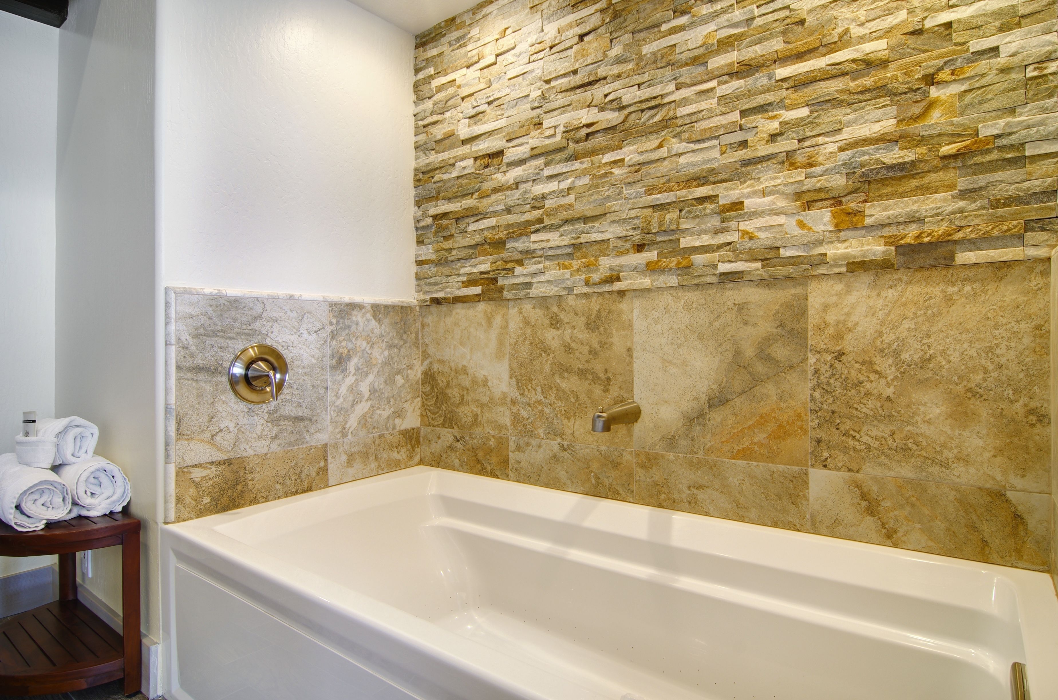 A bathroom with a stone wall, a bathtub, and a towel rack with towels.