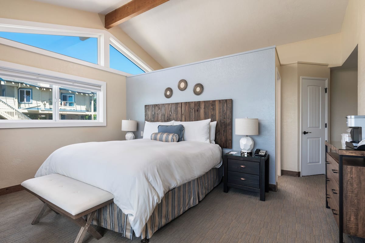 A bedroom with a large bed, bedside tables, a bench, and a view of a building outside.