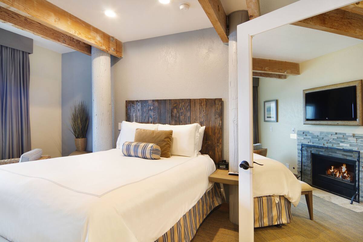 A bedroom with a large bed, wooden headboard, a fireplace, and a television on the wall.