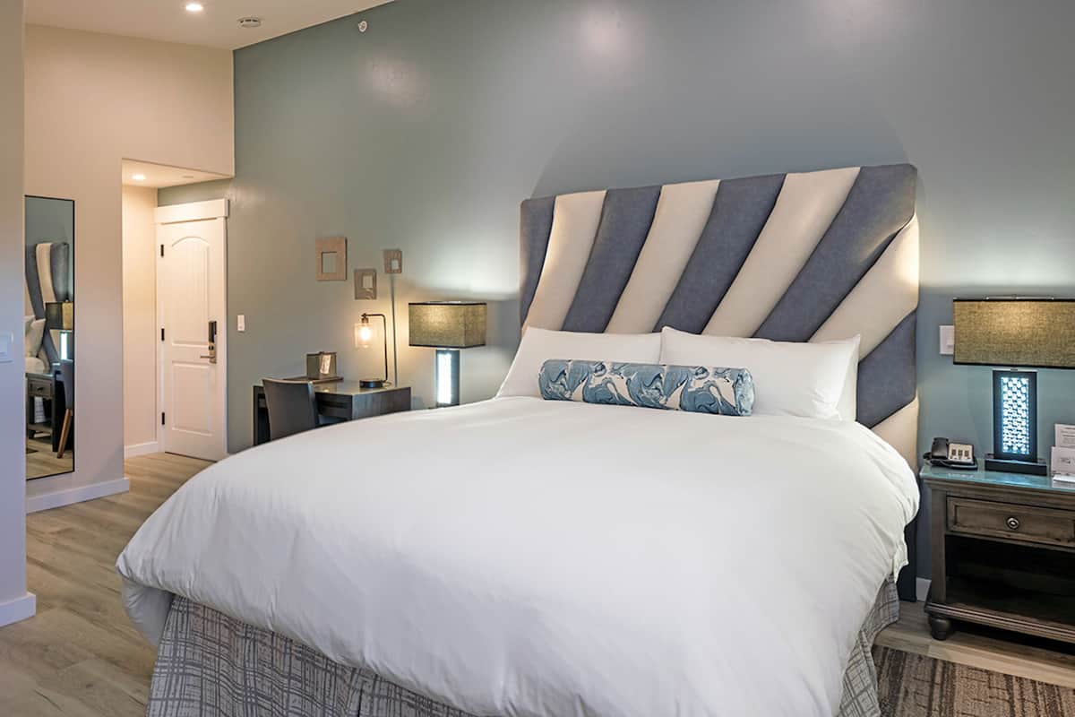 A large bed with a striped headboard, a bedside table with a lamp, and a mirror on the wall.