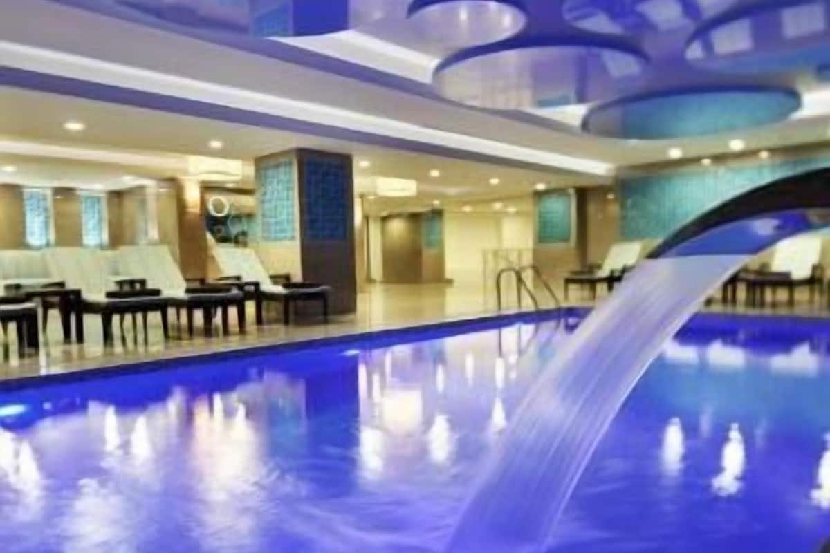 An indoor swimming pool with a blue hue, a modern ceiling design, and lounge chairs along the side.