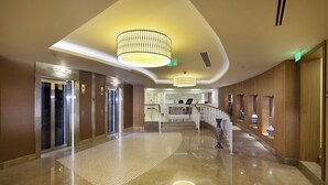 Un vestíbulo amplio con piso de mármol pulido, una imponente escalera y un moderno candelabro.