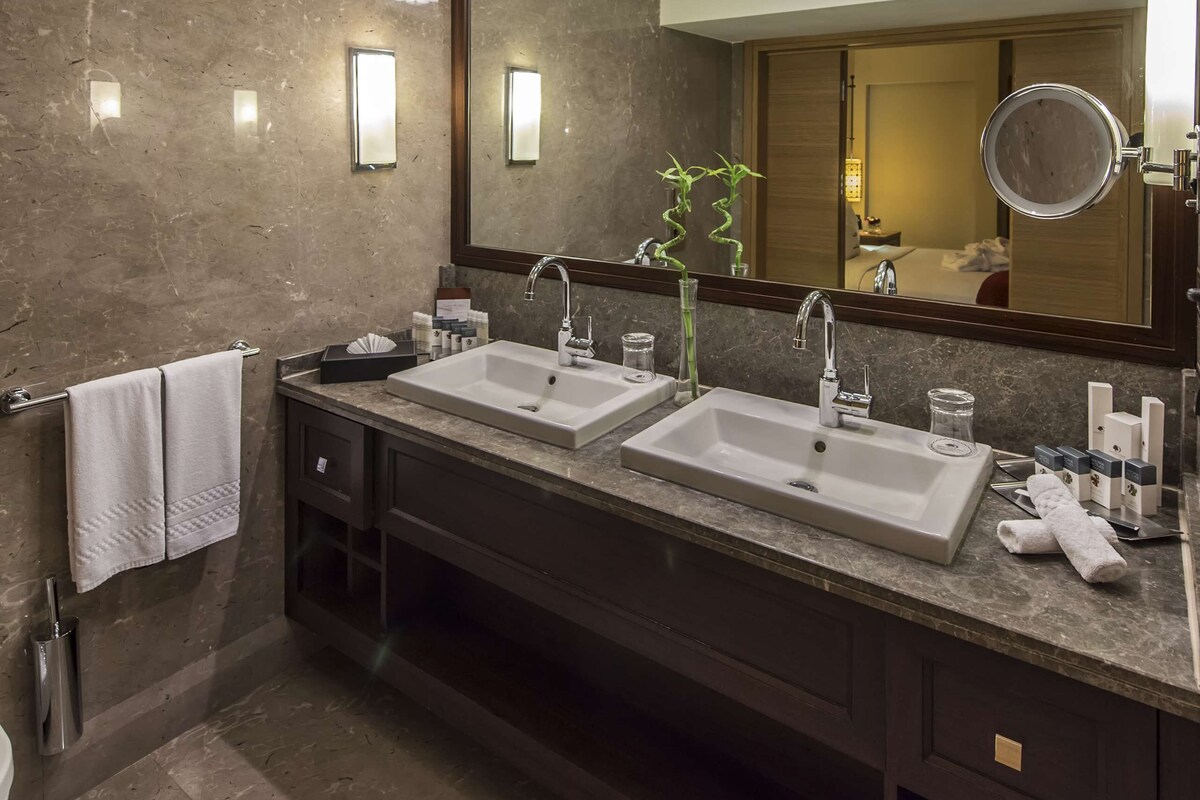 Une salle de bain moderne avec deux lavabos, un grand miroir et un luminaire au plafond.