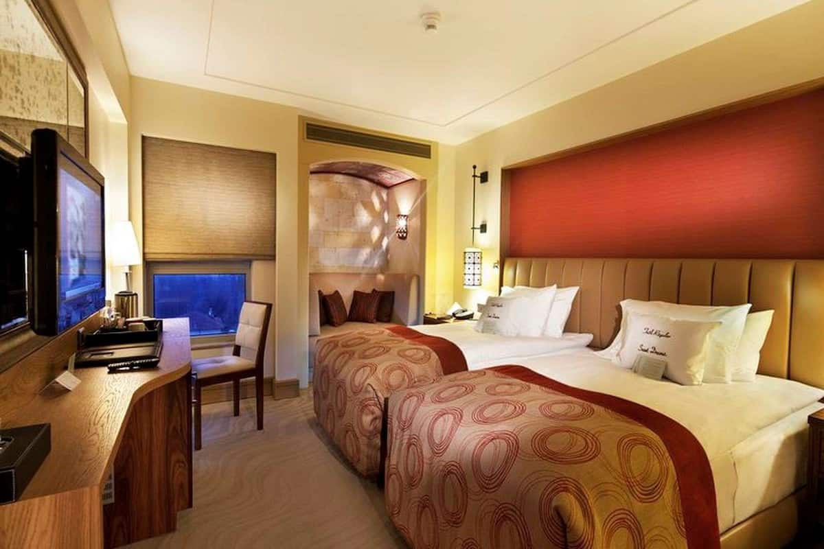 Een hotelkamer met een bureau, twee bedden, een televisie en een raam.