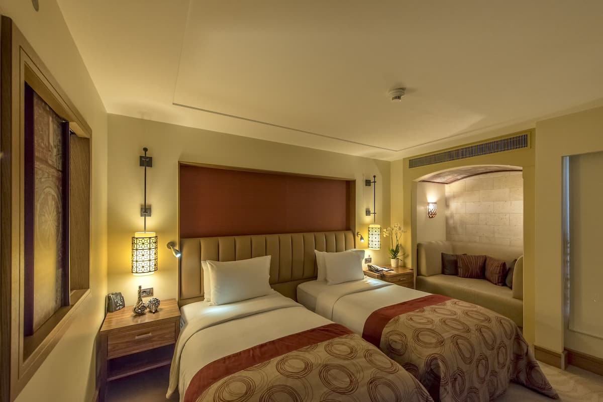 Een hotelkamer met twee bedden, een groot hoofdbord, nachtlampen, een nachtkastje en een bank.