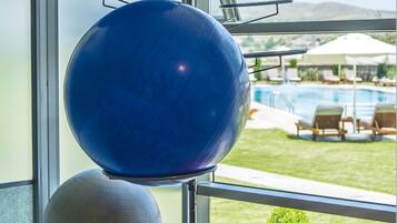 Pelotas de ejercicio en un soporte junto a una ventana con vistas a una zona de piscina.