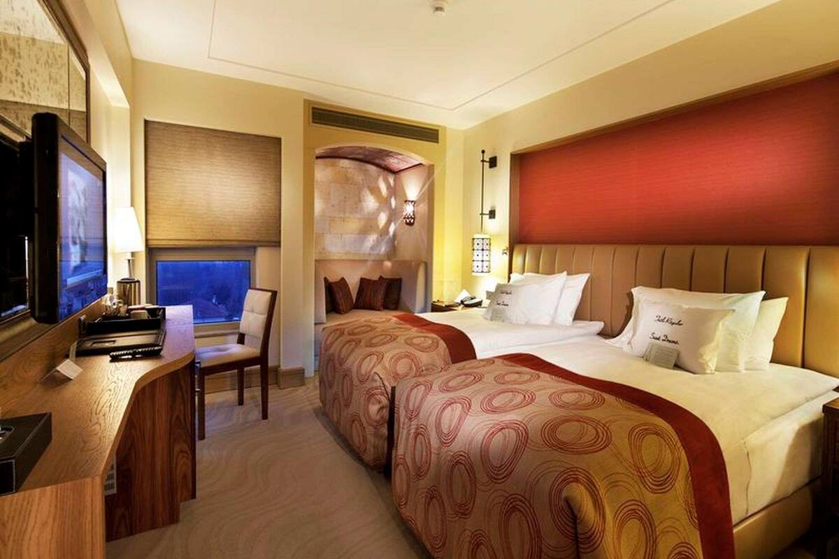 Een hotelkamer met een bureau, twee bedden, een televisie en een raam met zonwering.