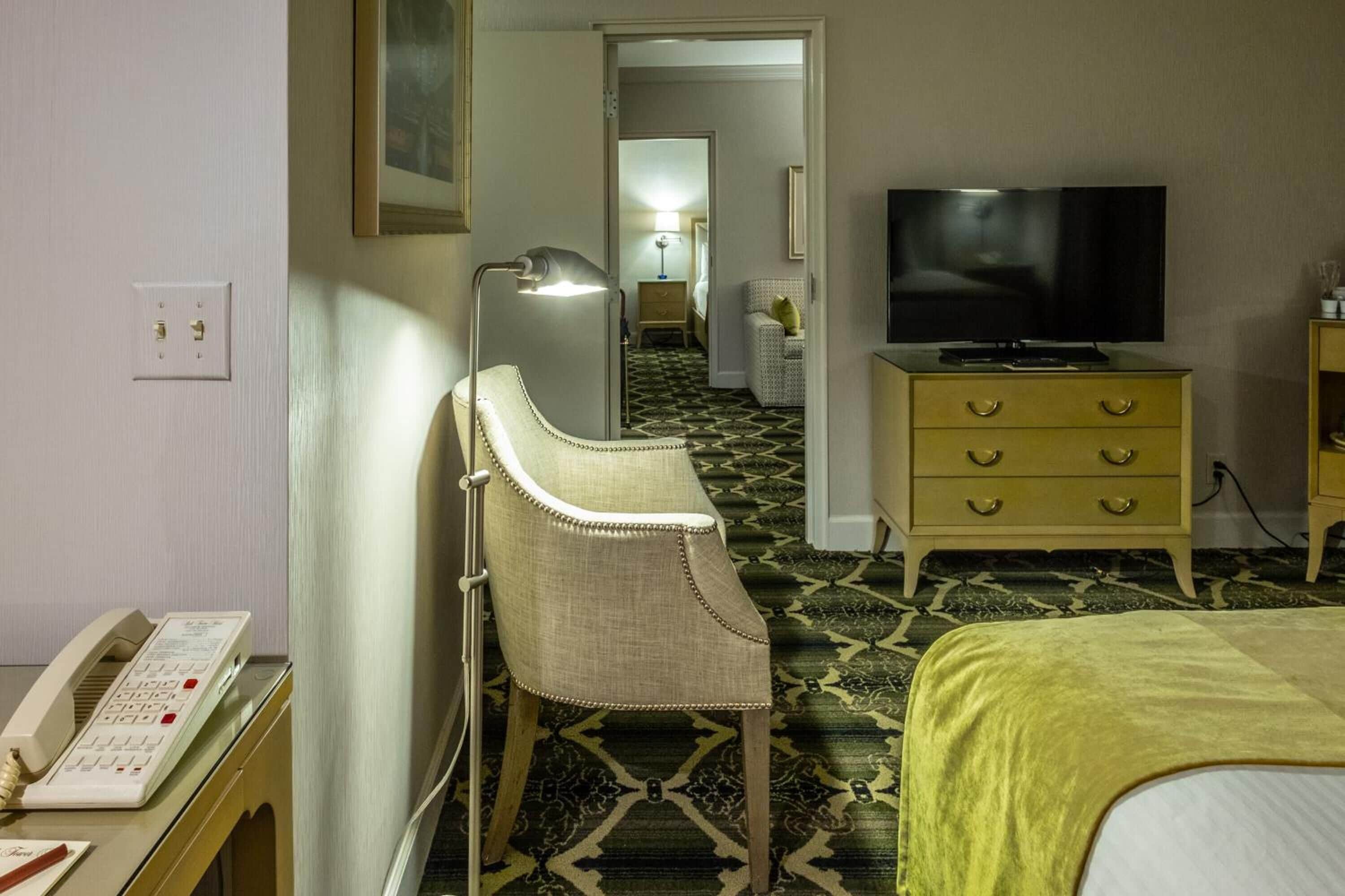 Una habitación de hotel con una cama, televisor, escritorio y teléfono, y una silla.
