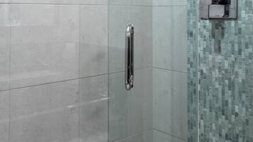 A shower area with a glass door, a shelf with toiletries, and a tiled wall with a mosaic pattern.