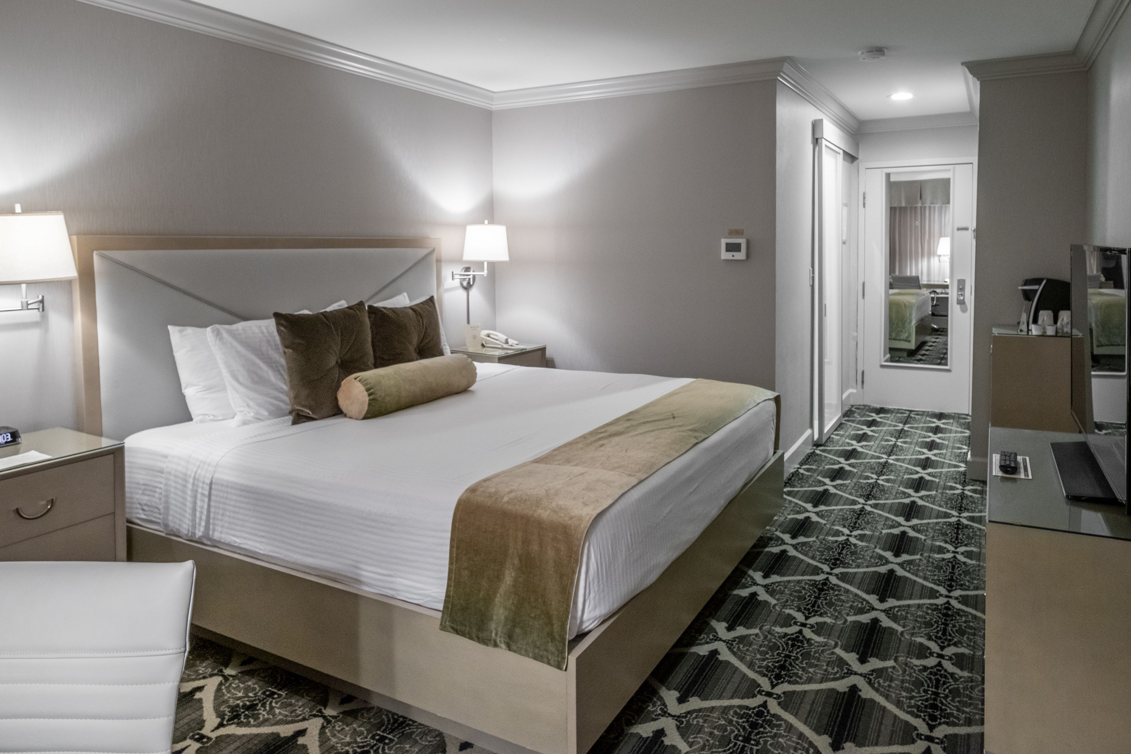 Een hotelkamer met een groot bed, nachtkastjes, een bureau en een spiegel.