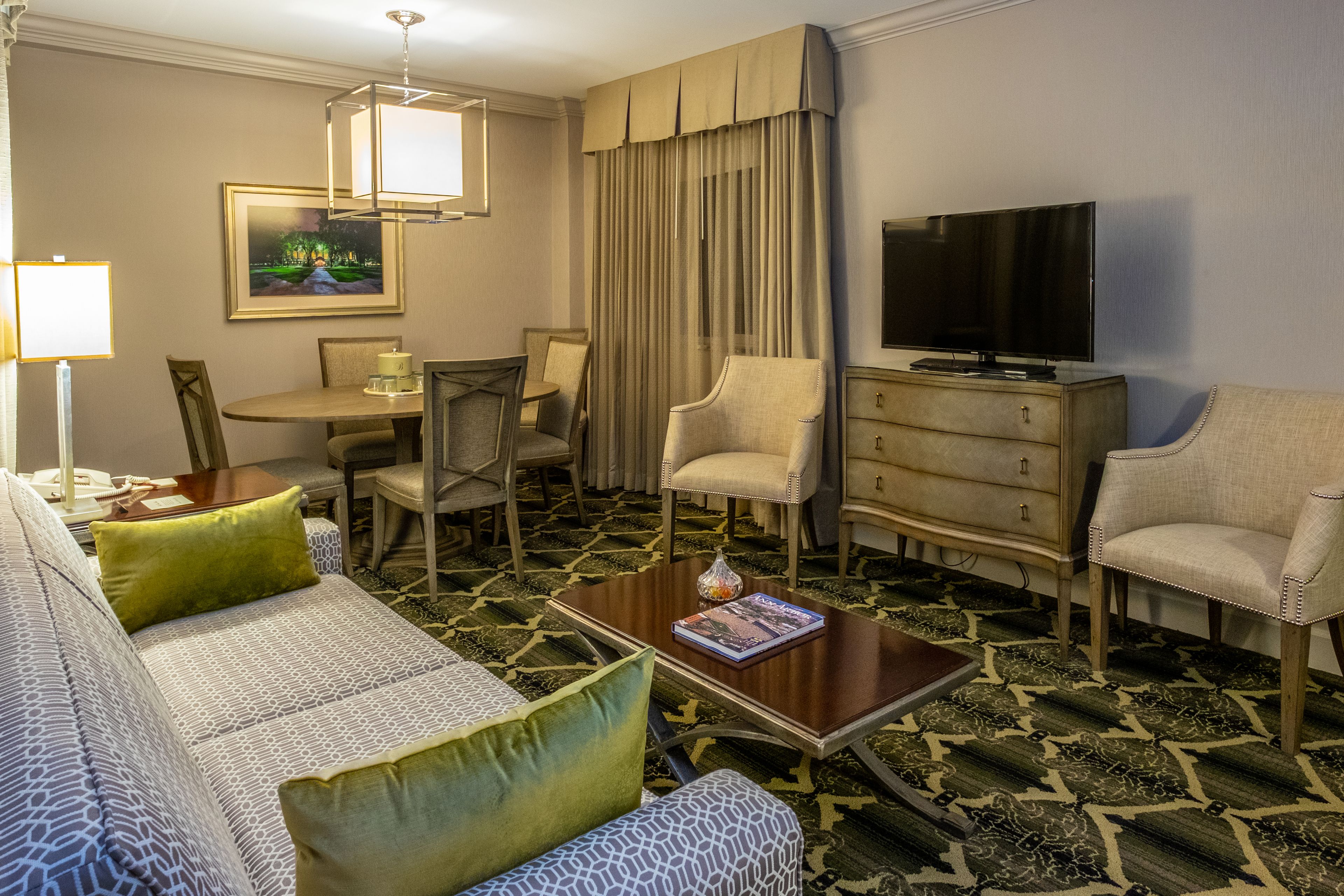 Una habitación de hotel con sofá, sillón, mesa de comedor y televisión.