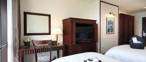Una habitación de hotel con una cama, un escritorio con lámpara, un televisor y un armario.