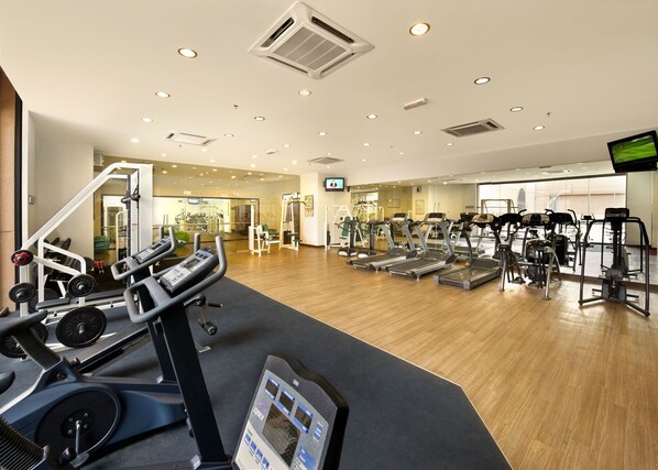Un gimnasio con cintas de correr, máquinas de pesas y un espejo grande.