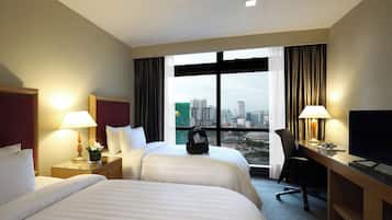 Une chambre d’hôtel avec deux lits, un bureau, une chaise, une télévision et une grande fenêtre donnant sur la ville.