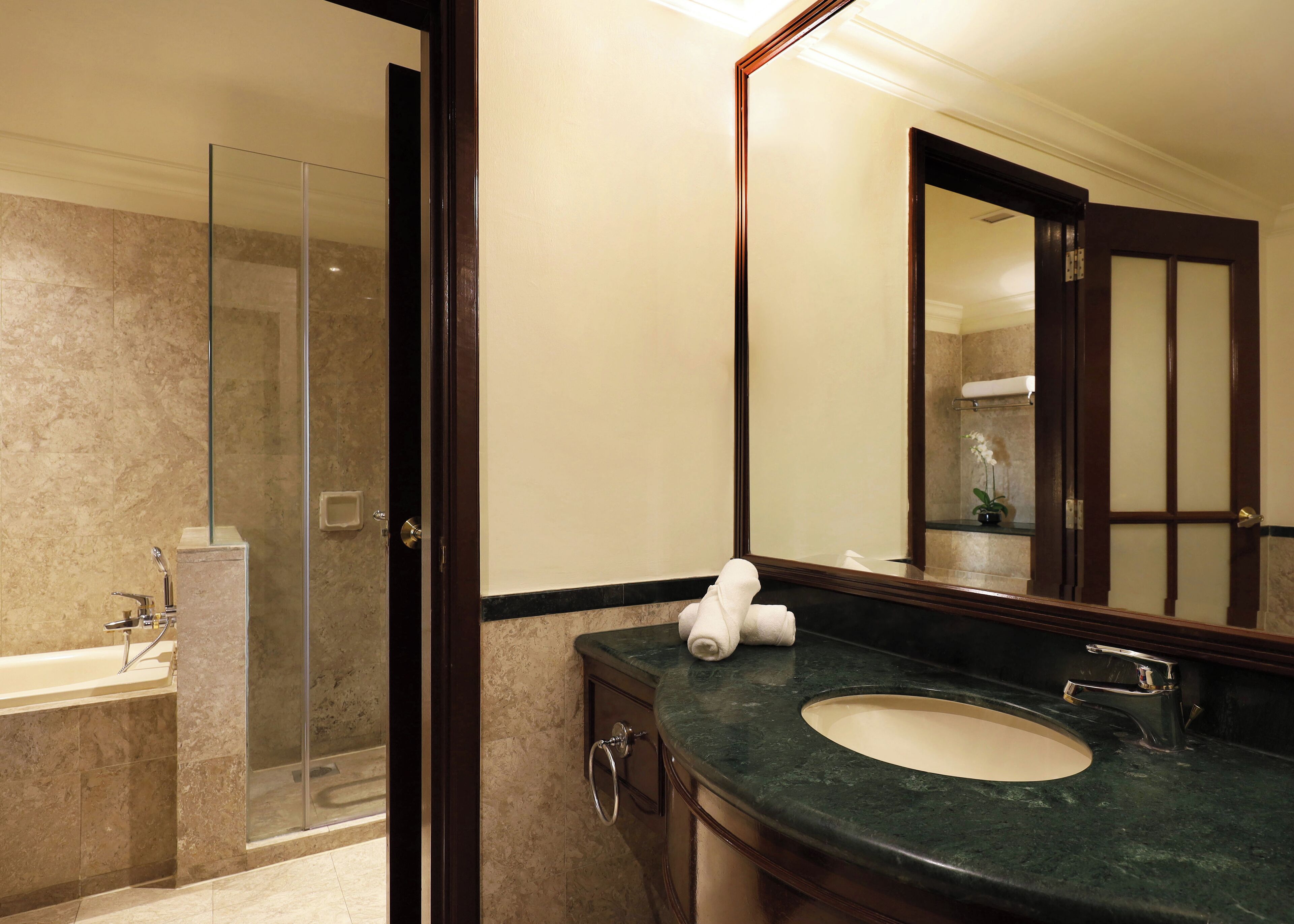 A modern bathroom with a glass shower enclosure, a sink with a marble countertop, and a large mirror.