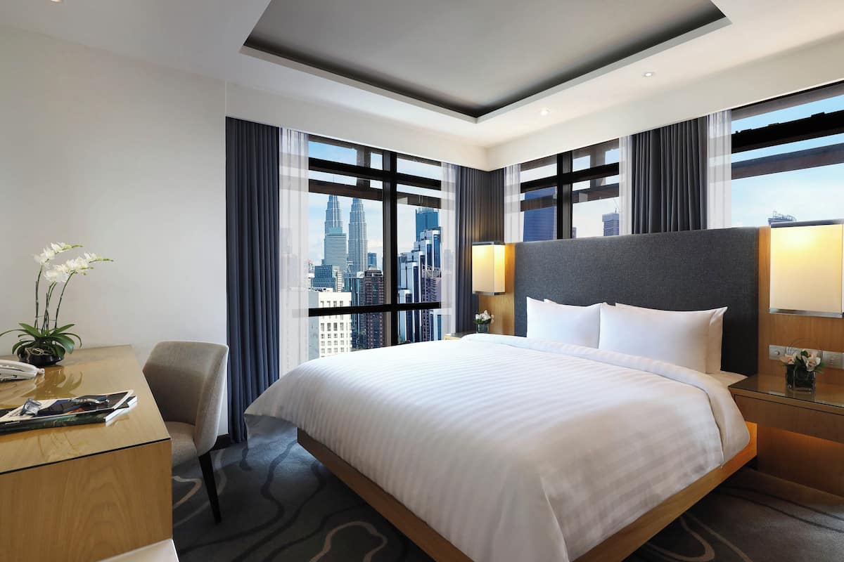 Une chambre d’hôtel moderne, dotée d’un grand lit, d’un bureau et offrant une vue sur le paysage urbain.