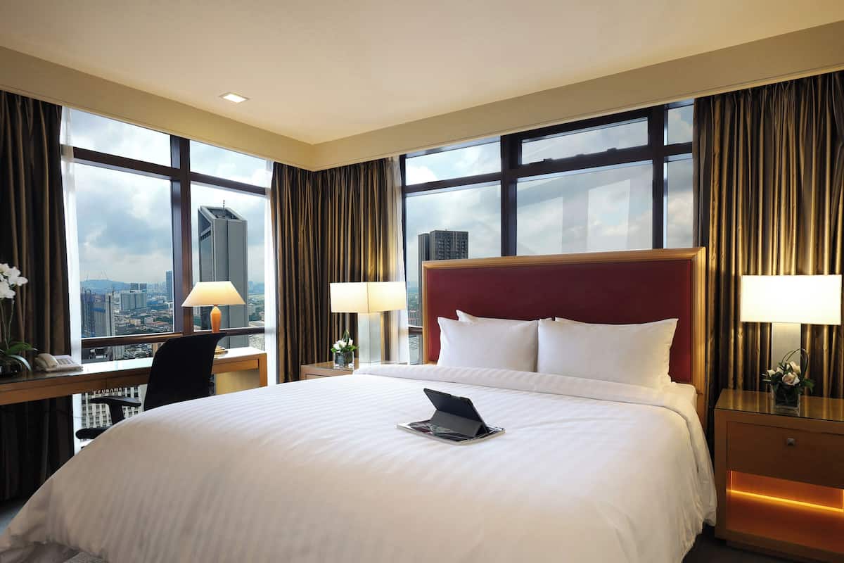 Une chambre d’hôtel dotée d’un grand lit, de deux tables de chevet avec des lampes, d’un bureau avec une chaise et offrant une vue sur la ville grâce à de grandes fenêtres.