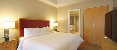 Habitación de hotel con una cama grande, lámparas de noche, televisión, armario de madera y baño visible a través de una puerta abierta.