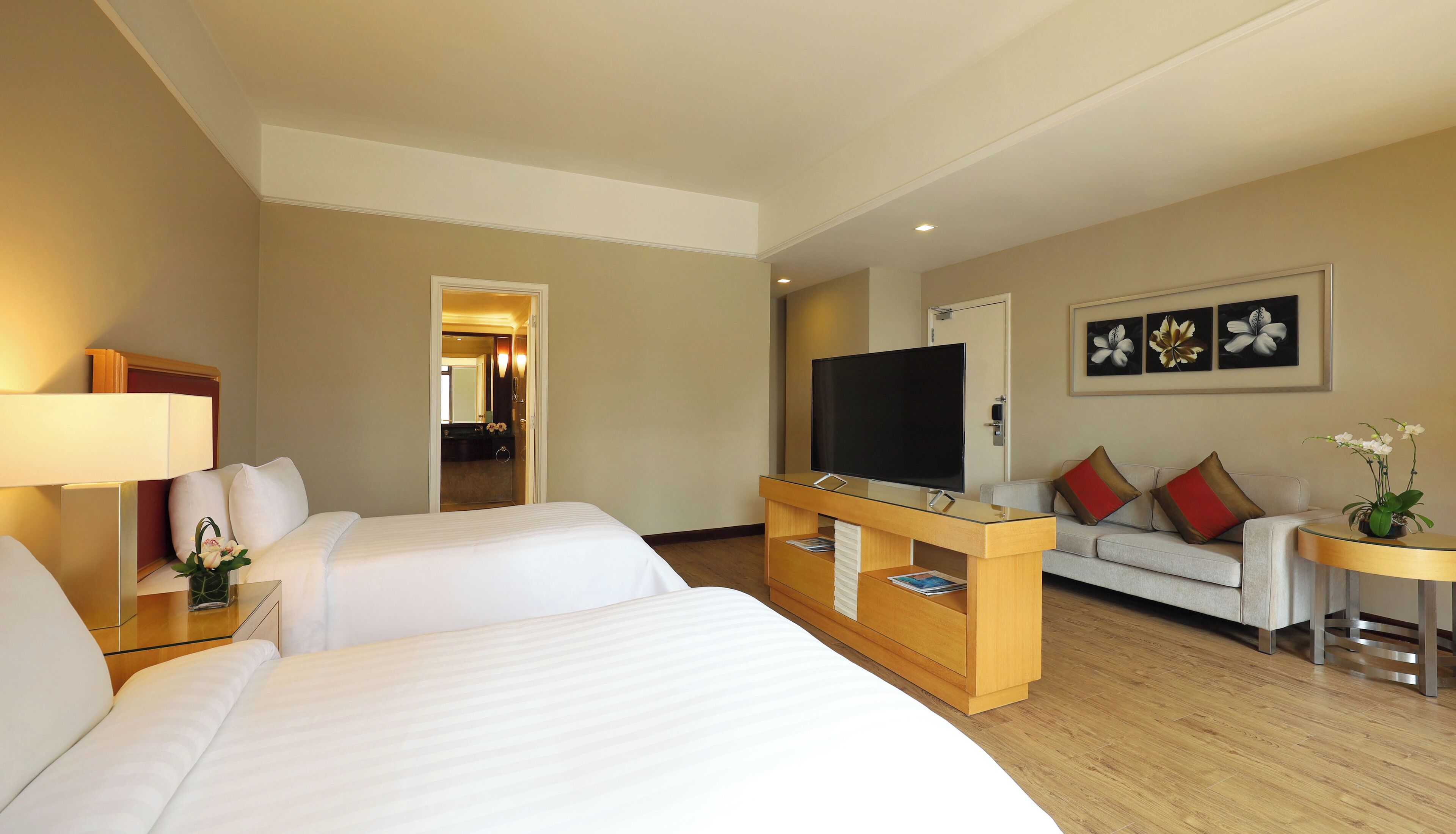 A hotel room with two beds, a TV, a sofa, and a small table with a lamp.