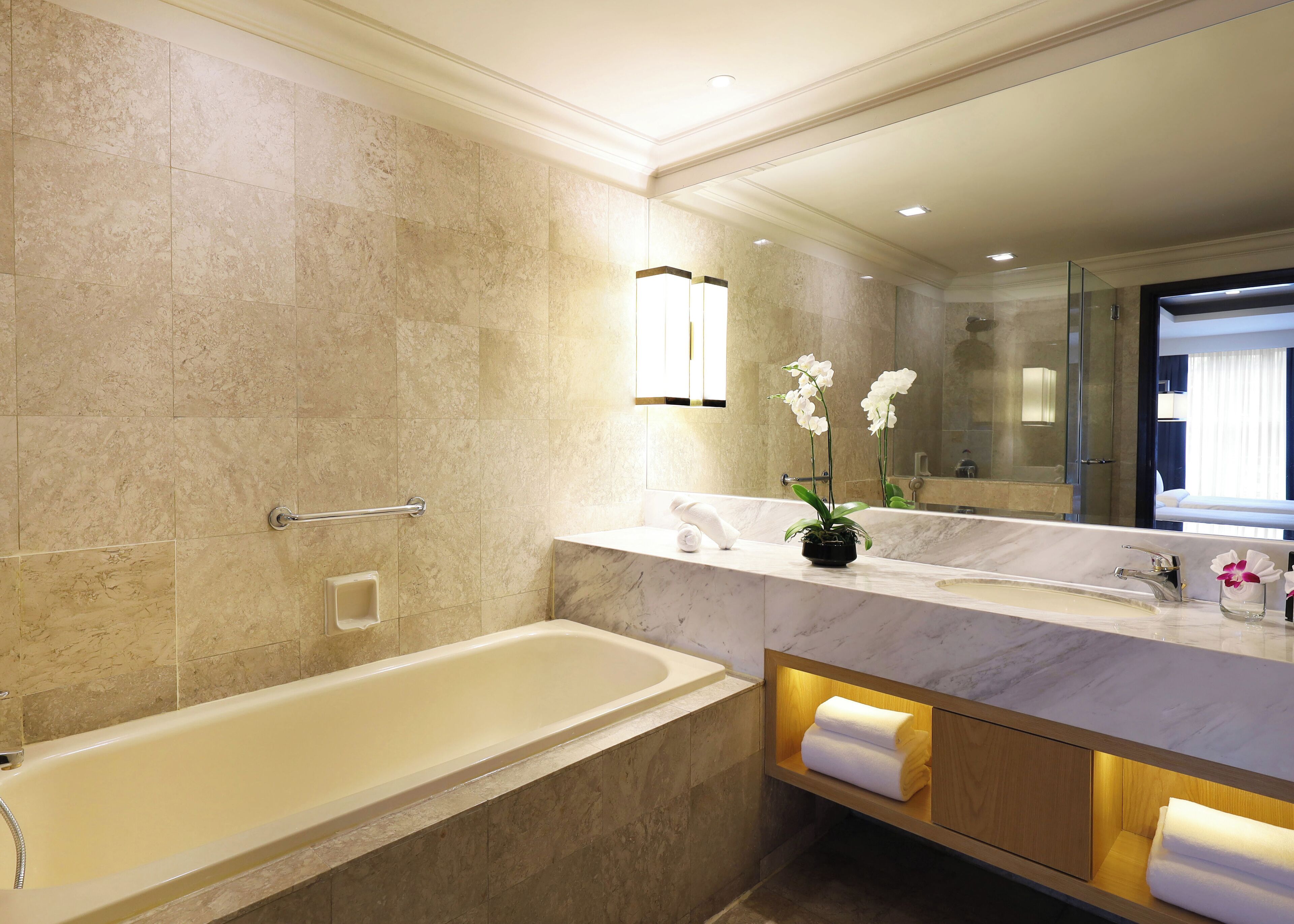 Ein modernes Badezimmer mit einer Badewanne, einem Waschtisch mit Spiegel und einer Zimmerpflanze, einer Orchidee.