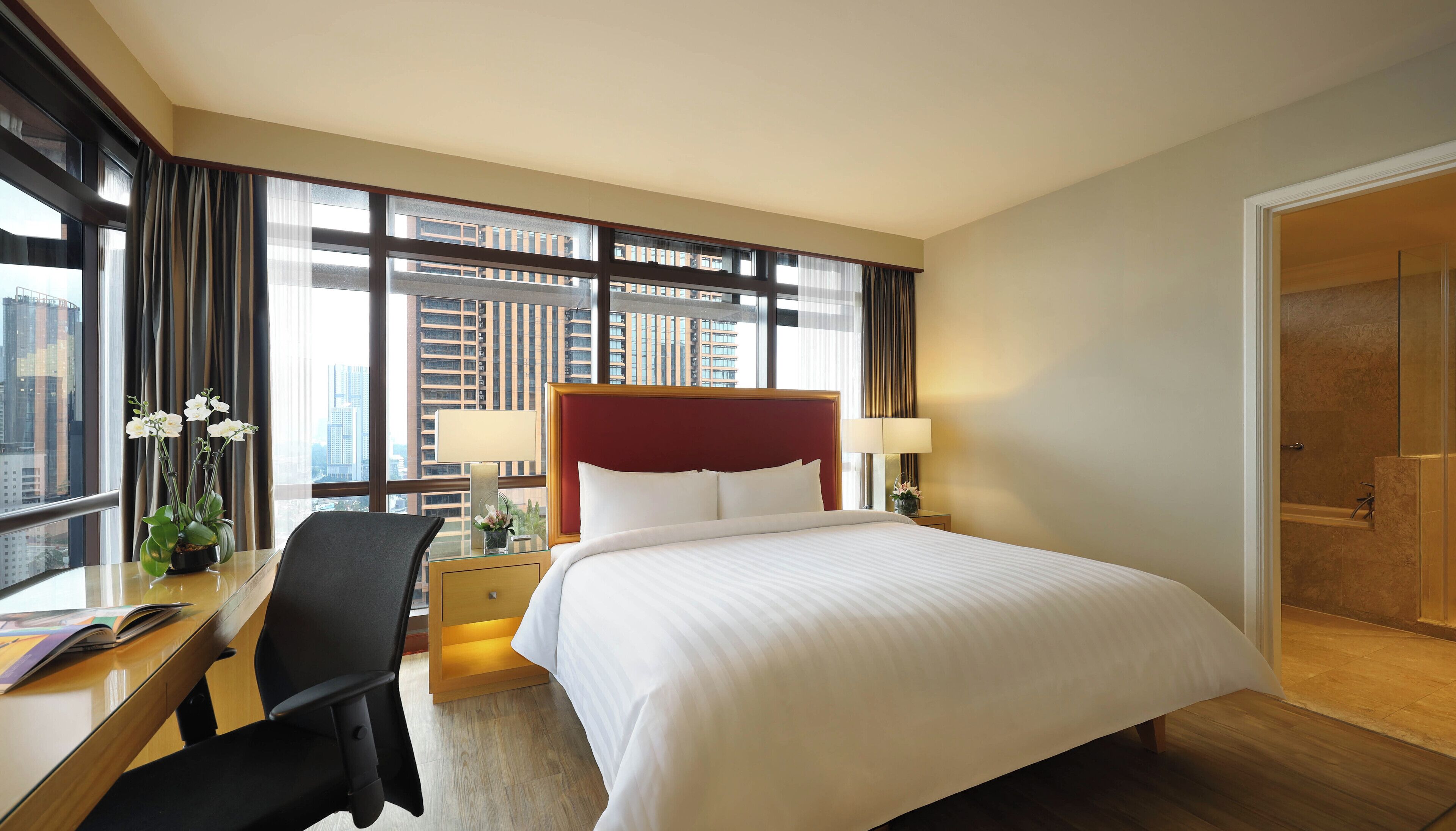 Ein Hotelzimmer mit einem großen Bett, einem Schreibtisch mit Stuhl, einem Nachttisch und einem durch eine offene Tür einsehbaren Badezimmer.