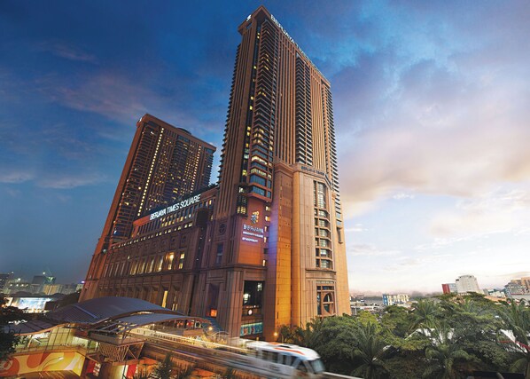 Een hoog hotel met meerdere verdiepingen, een opvallend bord met de tekst 'BERJAYA TIMES SQUARE' en een uitzicht op de omliggende stad.