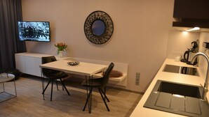 Une cuisine moderne avec un plan de travail blanc, des chaises noires, une petite table à manger et un téléviseur fixé au mur.