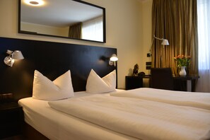 A hotel room with a large bed, two bedside lamps, a nightstand, a desk, and a mirror on the wall. - Hotel Belle Blue (Munich)