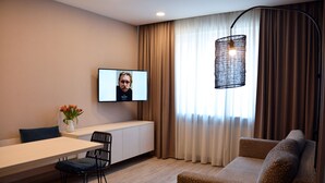 Un salon moderne avec un canapé, une table à manger et des chaises, un téléviseur fixé au mur et une fenêtre avec des rideaux.