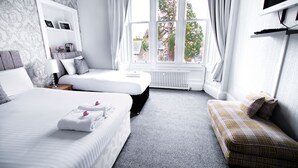 A hotel room with two beds, a sofa, a TV, and a window with a view of trees and houses. - McInnes House rooms with breakfast (Kingussie)