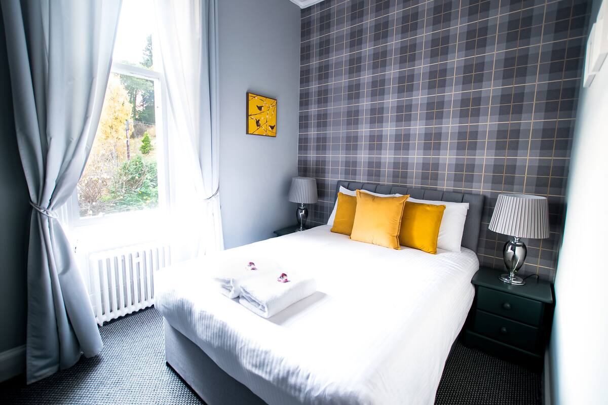 A neatly arranged hotel room with a large bed, a bedside table with lamps, and a window with curtains.