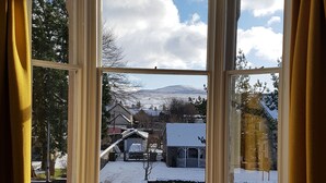 A room with a large bay window overlooking a snowy landscape, a wooden desk, and a radiator. - McInnes House rooms with breakfast (Kingussie)