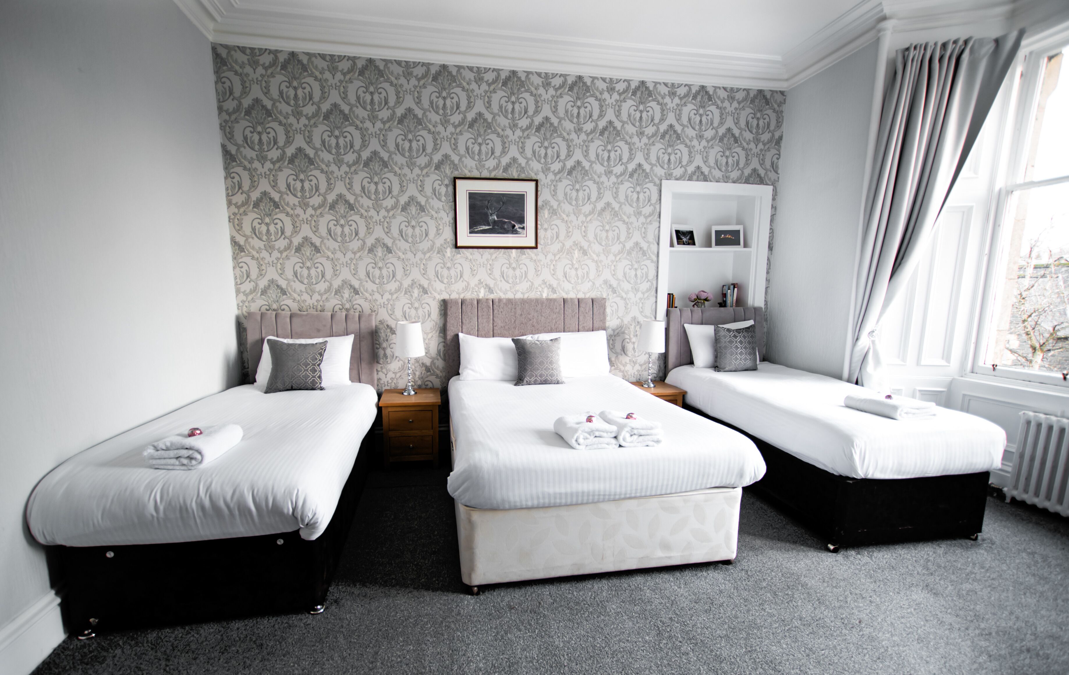 A hotel room with two single beds, a nightstand with a lamp, a dresser, and a window with curtains.
