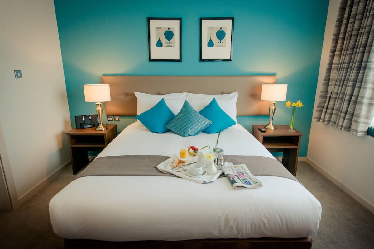 A neatly made bed with a tray of breakfast items, two bedside lamps, and a vase of flowers.