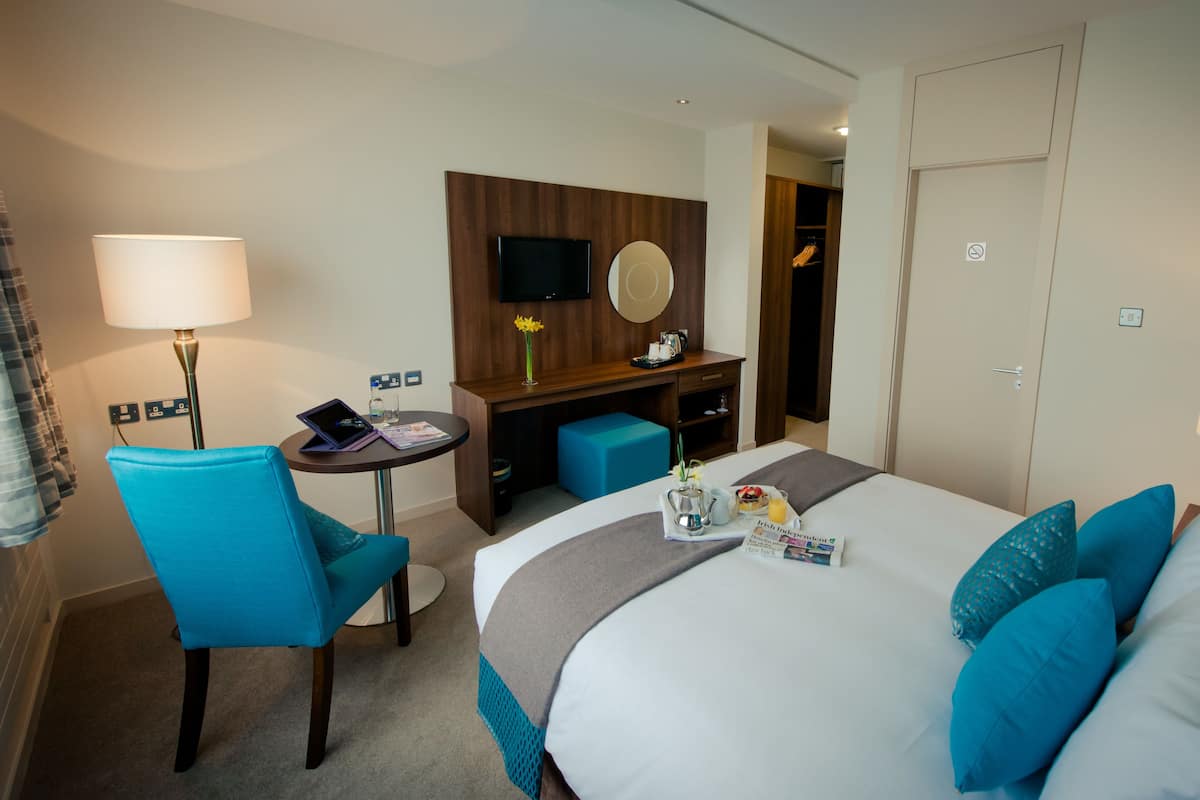 A hotel room with a bed, a desk, a chair, a TV, and a wardrobe.