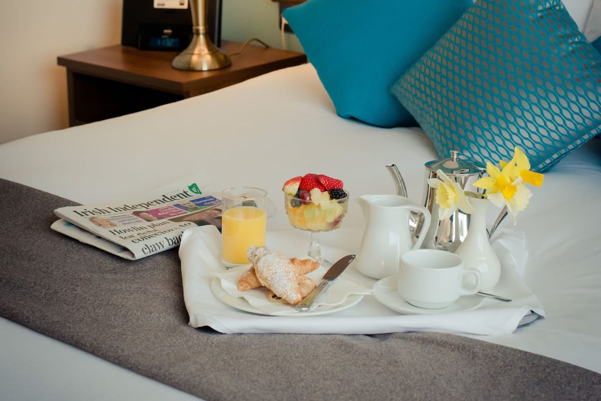 A neatly made bed with a tray of breakfast items, including croissants, fruit, and a cup of coffee.