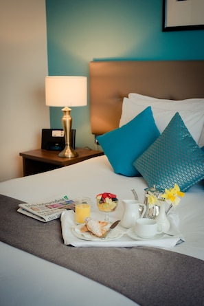 A neatly made bed with a tray of breakfast items, including croissants, fruit, and a cup of coffee. - IMI Conference Centre & Residence (Dublin)