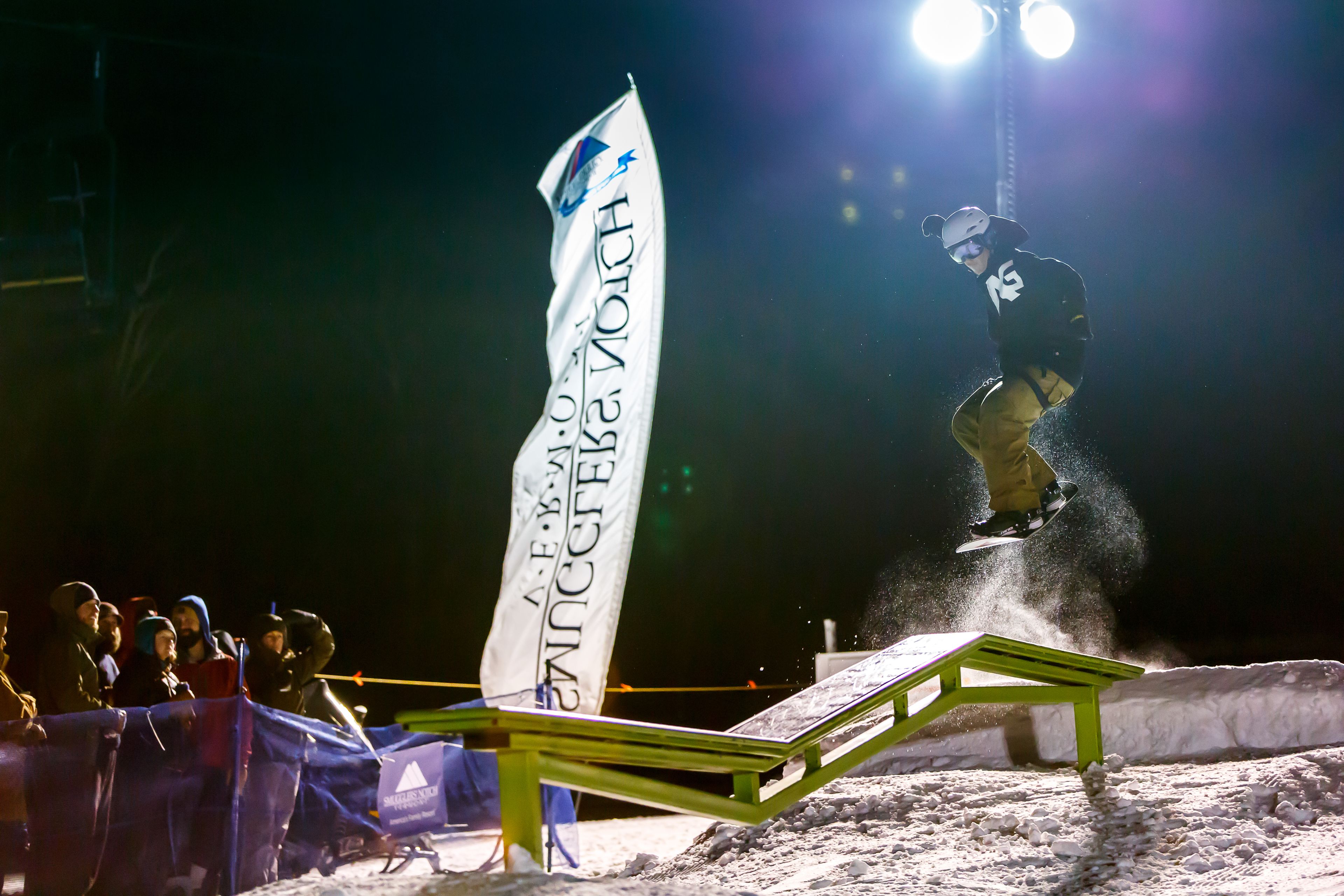 Ein Snowboarder vollführt einen Trick über eine Metallschine bei einem Nacht-Event.