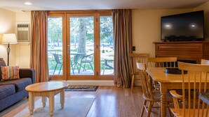 A living room with a sofa, a coffee table, a TV on a wooden cabinet, and a dining area with a table and chairs. - Smugglers' Notch Resort (Jeffersonville)