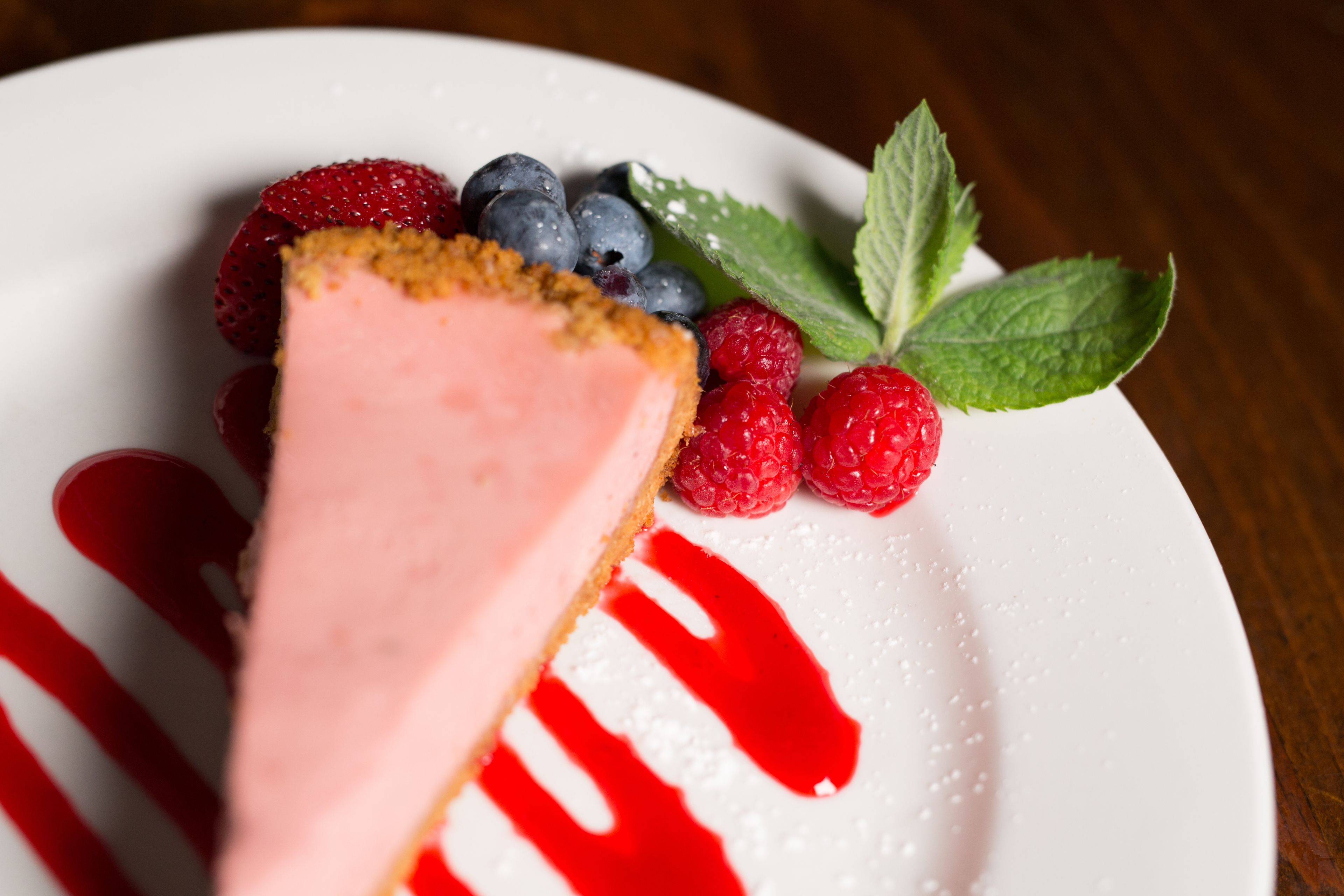 A slice of cheesecake with berries and mint on a white plate.