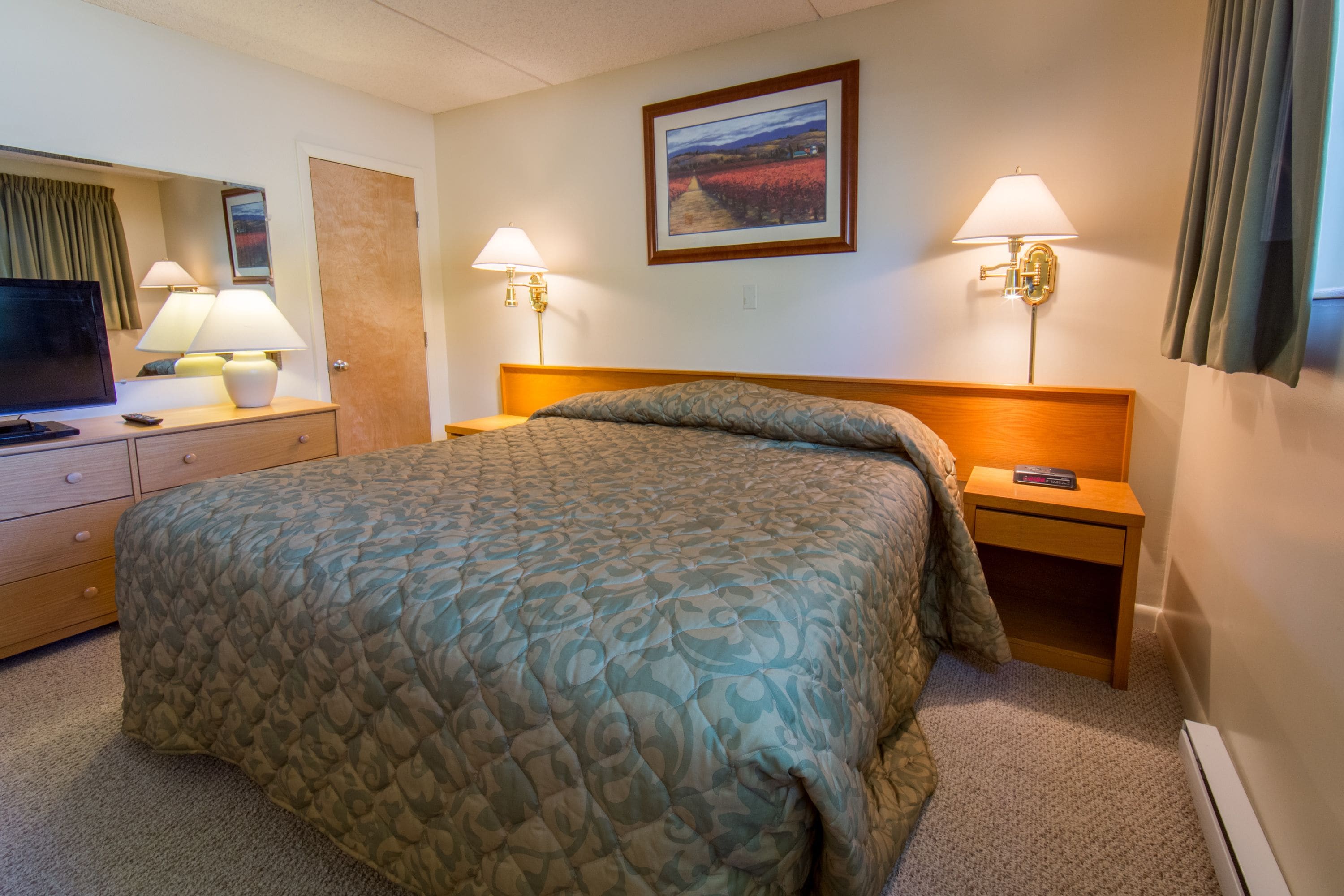 Une chambre d’hôtel équipée d’un lit, d’un bureau, d’une télévision et de deux lampes de chevet.
