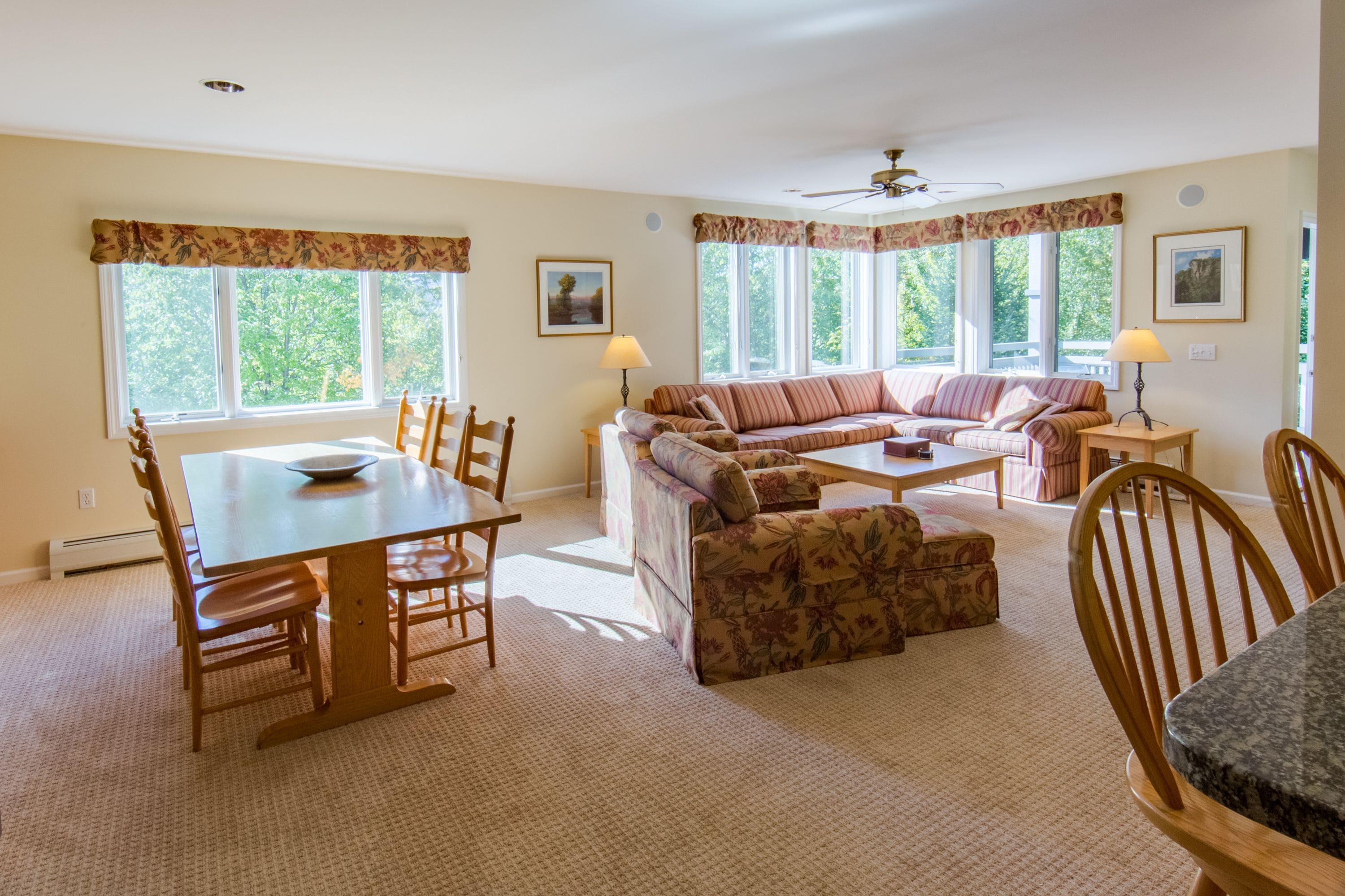 A spacious living room with a sofa set, a dining table with chairs, and a ceiling fan.