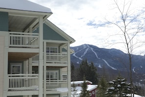 A multi-story building with balconies, a mountain view, and snow-covered trees. - Smugglers' Notch Resort (Jeffersonville)