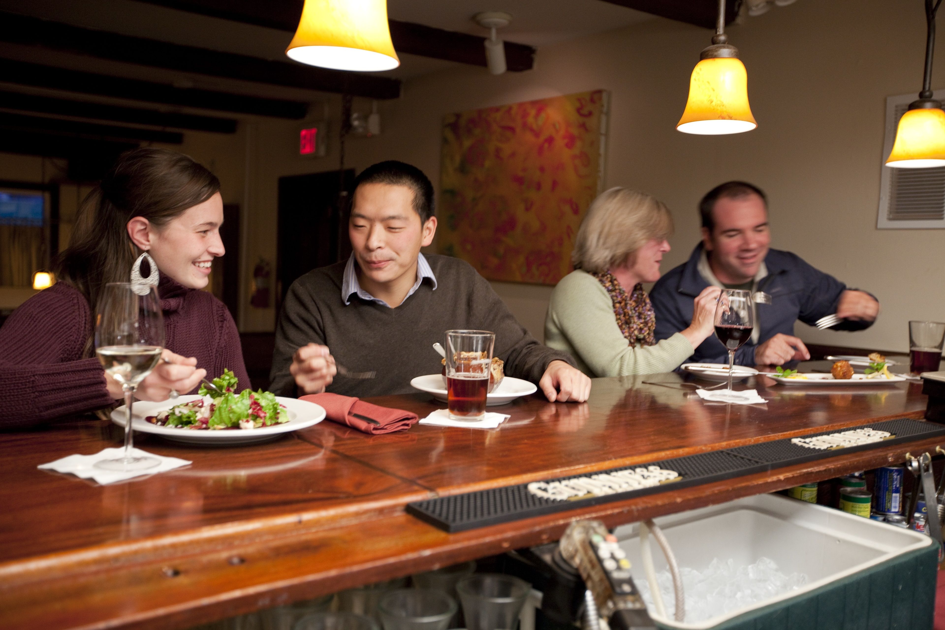 A group of people dining at a restaurant with wooden tables and yellow pendant lights.