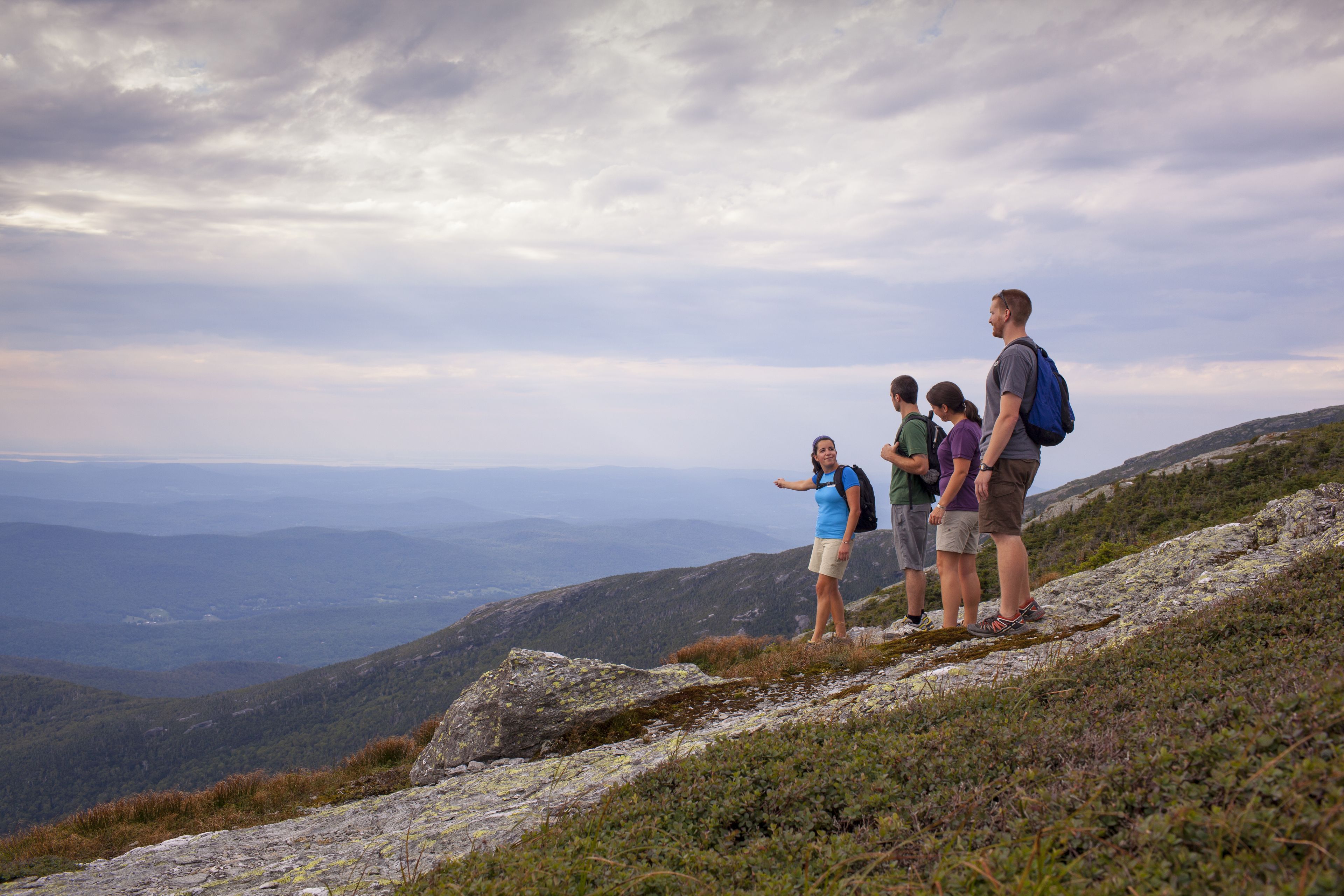 A group of people standing on a rocky mountain ridge with a view of distant mountains and valleys.