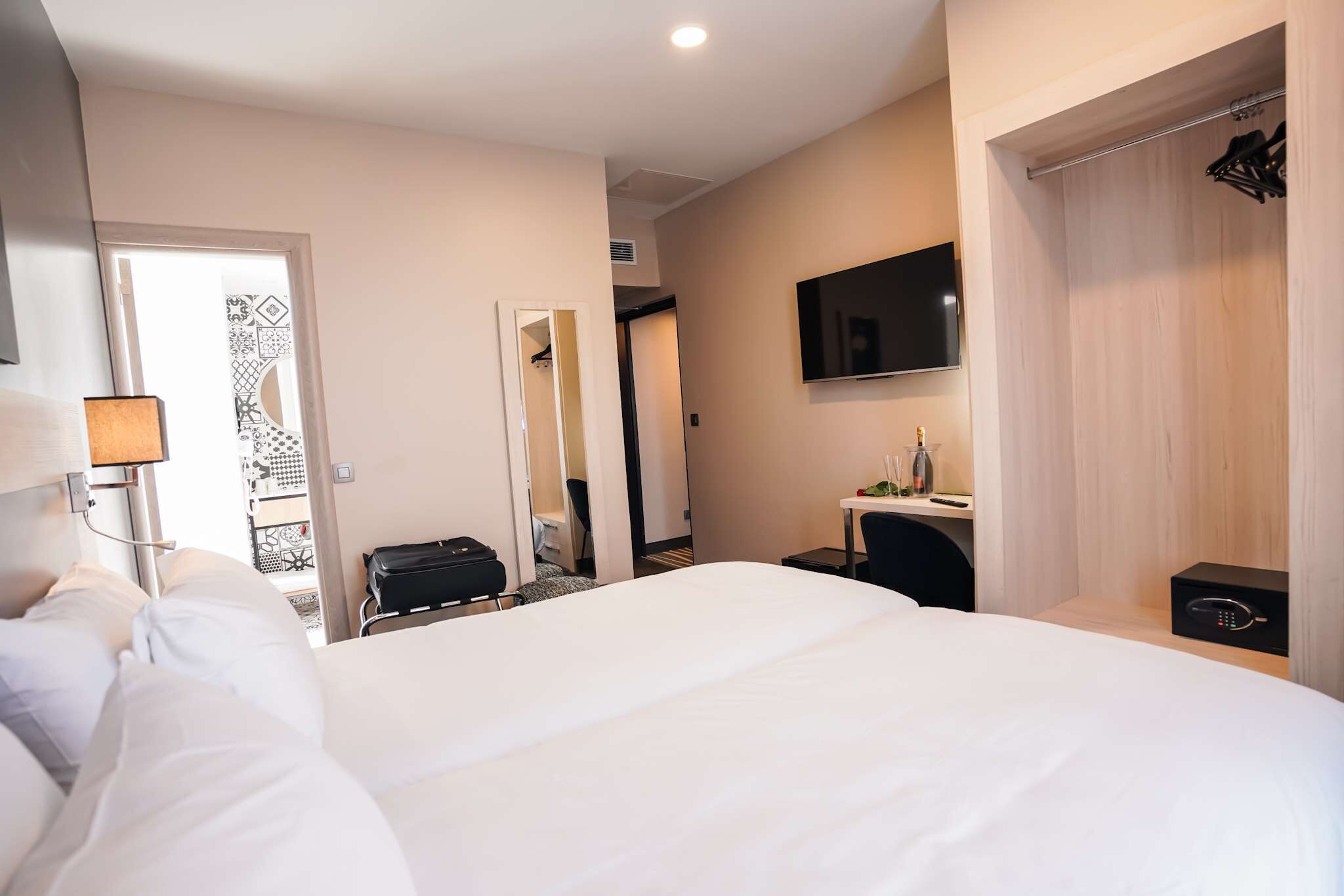 Une chambre d’hôtel avec un grand lit, un bureau avec une chaise, un téléviseur fixé au mur et un porte-manteau.