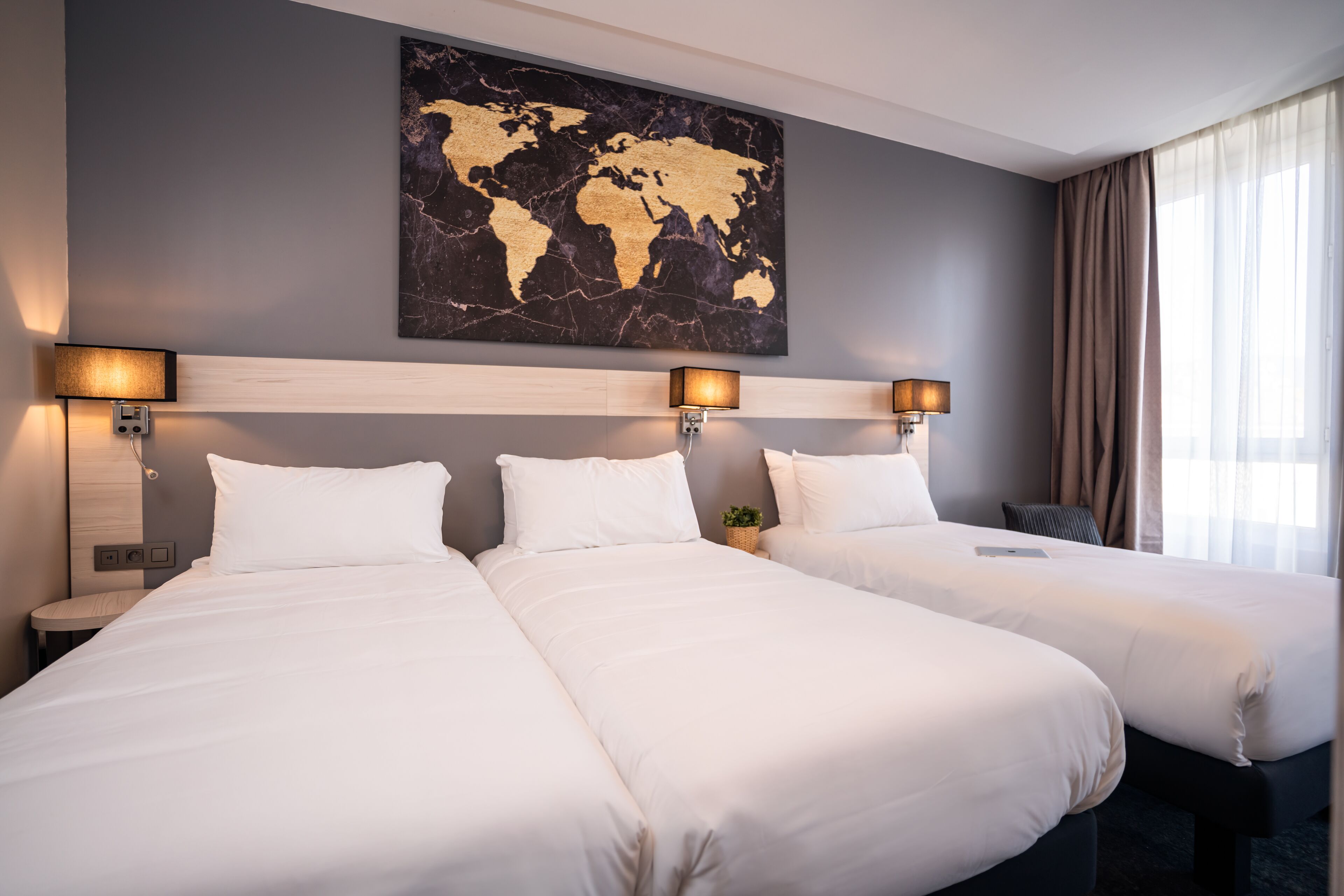 A hotel room with two beds, a world map artwork on the wall, and a large window with curtains.